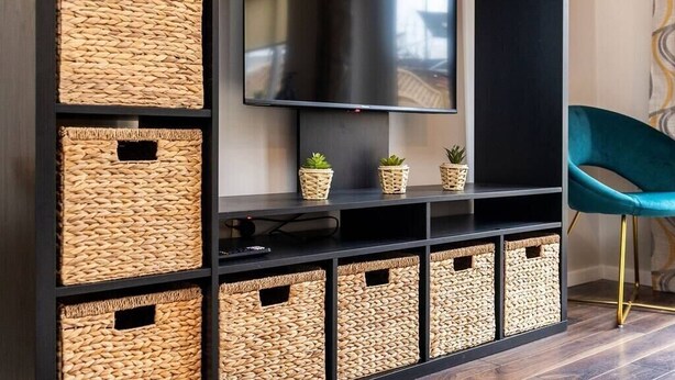 A modern entertainment unit with a flat-screen TV, woven baskets, and a teal chair. - Stunning 3 Bedroom Home Hillsborough Sheffield (Hillsborough)