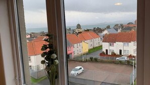 A window view of a residential area with houses, a road, and a distant church. - Superb One Bedroom Getaway in Dysart Kirkcaldy (Dysart)