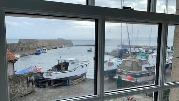 A view through a window of a harbor with boats docked, a stone wall, and a cobblestone ground. - Superb One Bedroom Getaway in Dysart Kirkcaldy (Dysart)