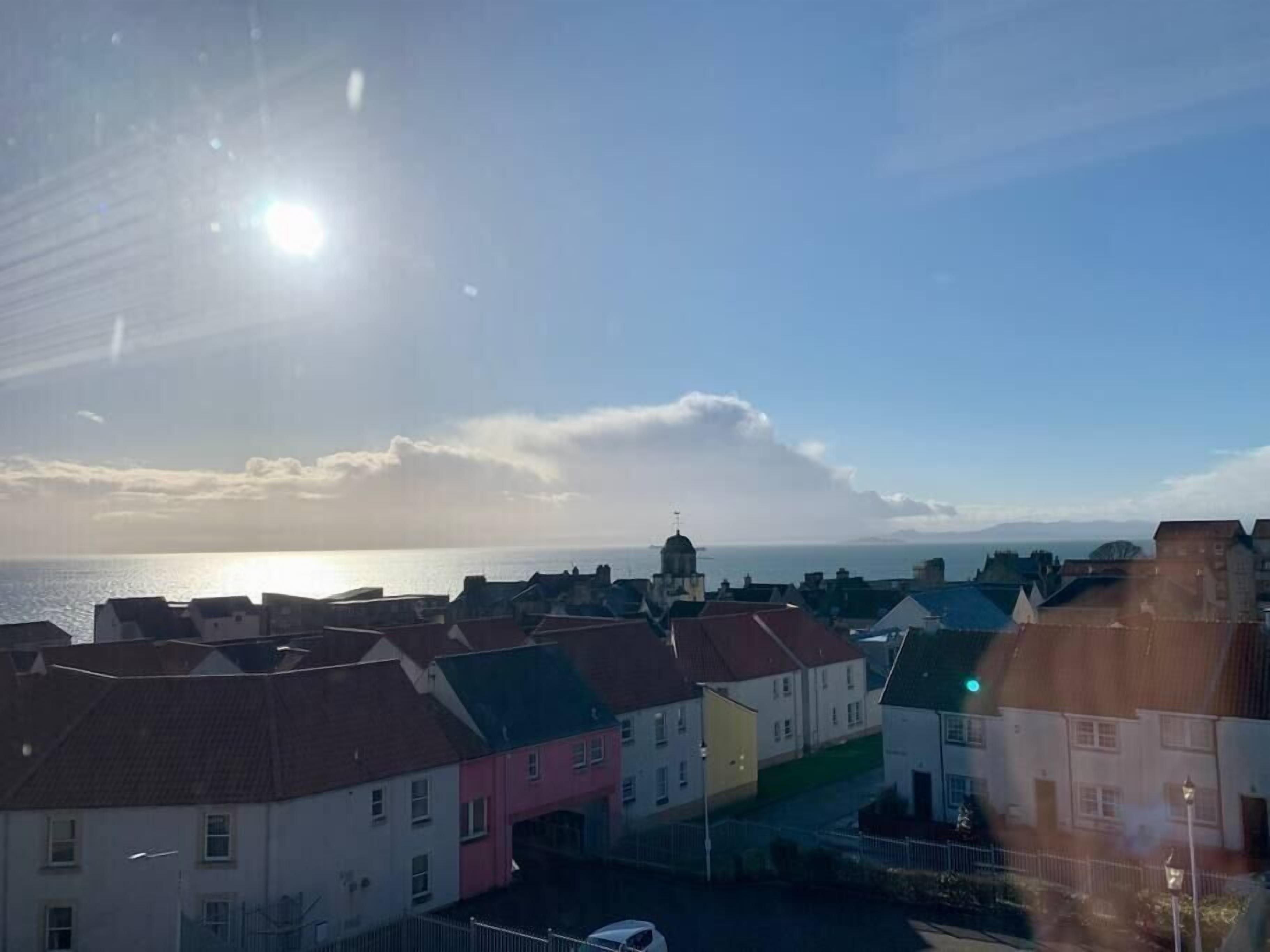 En kystby med pastelfarvede bygninger, en klar himmel og lav sol på horisonten.