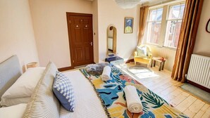 Une chambre d’hôtel avec un lit, une chaise, un bureau, un miroir et une fenêtre avec des rideaux.