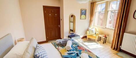 Une chambre d’hôtel avec un lit, une chaise, un bureau, un miroir et une fenêtre avec des rideaux.