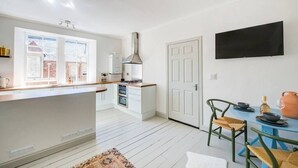 Une cuisine moderne avec des meubles blancs, un îlot central et un coin repas comprenant une table bleue et des chaises vertes.