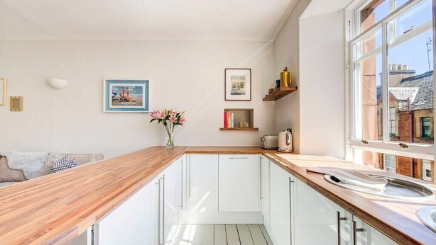 Une cuisine moderne avec des meubles blancs, un plan de travail en bois et une fenêtre donnant sur la ville.