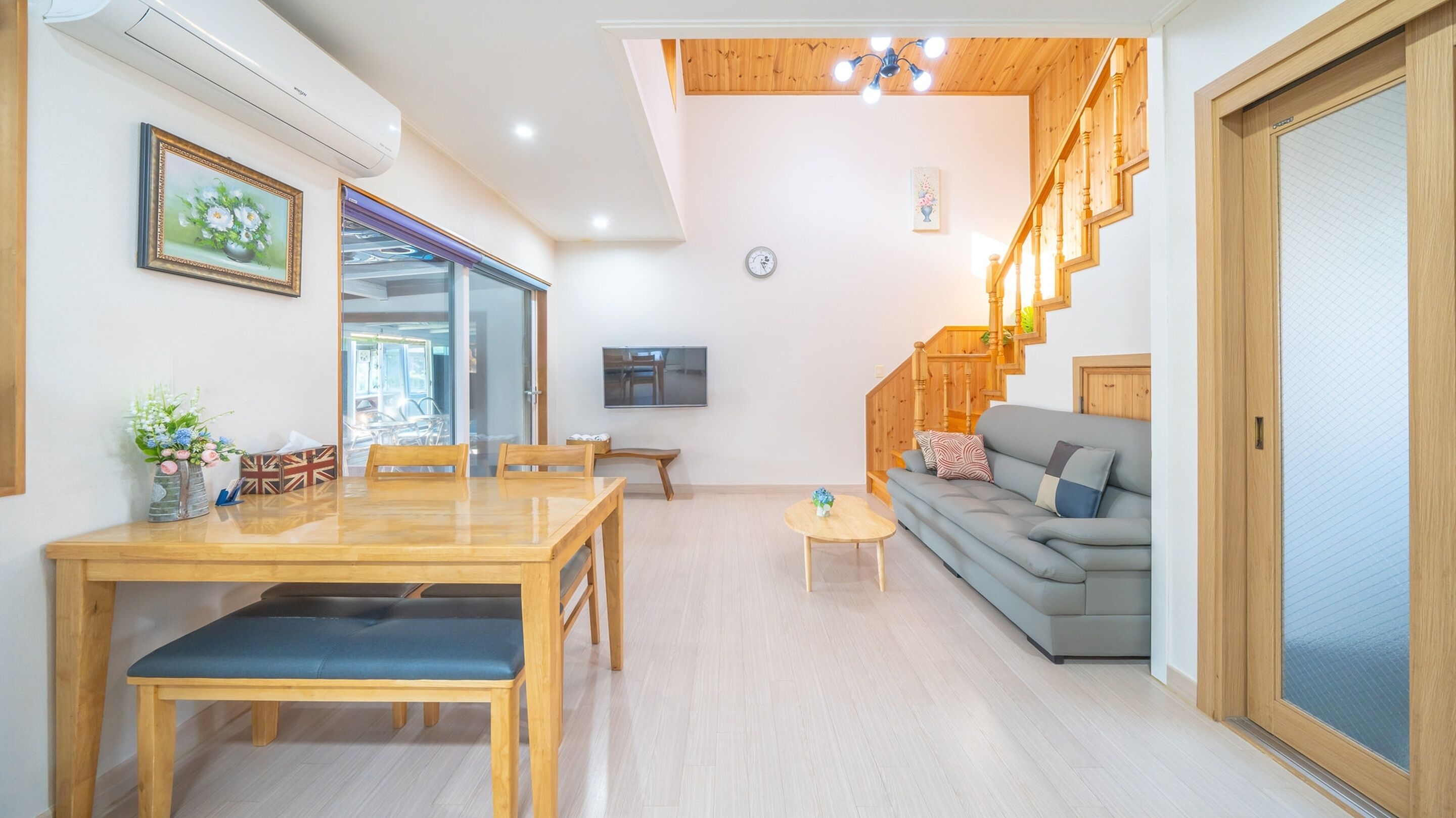 Un salon moderne avec une table à manger en bois, un canapé gris et un escalier avec des rampes en bois.