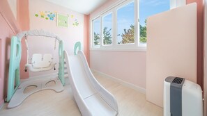 Un espace de jeux pour enfants avec un toboggan, des toilettes pour enfants et une fenêtre donnant sur les arbres.