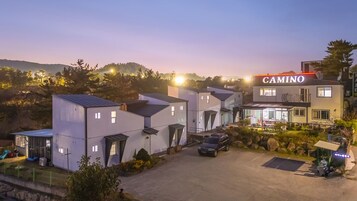 Un hotel moderno con un letrero que dice 'CAMINO', con estacionamiento y un pequeño jardín.