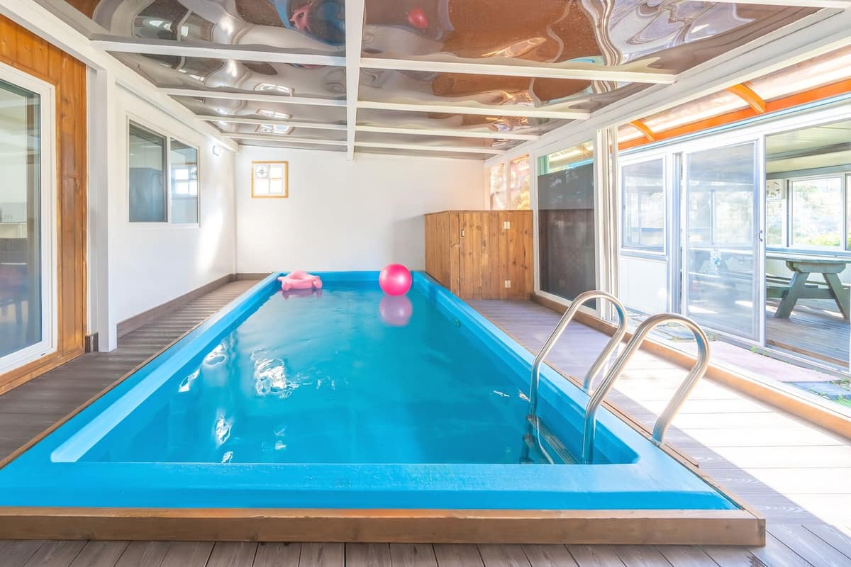 Una piscina interior con cubierta de madera, paredes de vidrio y techo con vigas a la vista.