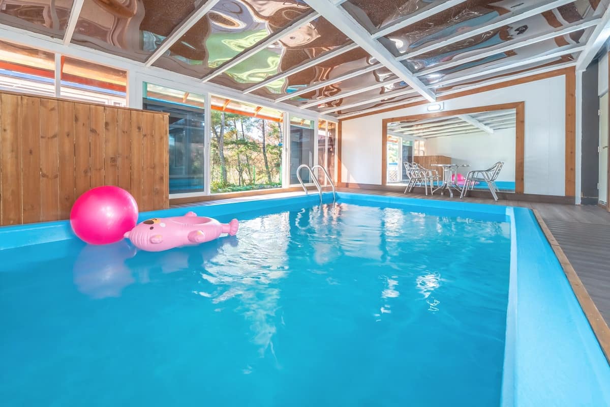 Una piscina interior con agua azul cristalina, paredes de madera y un techo de diseño único.