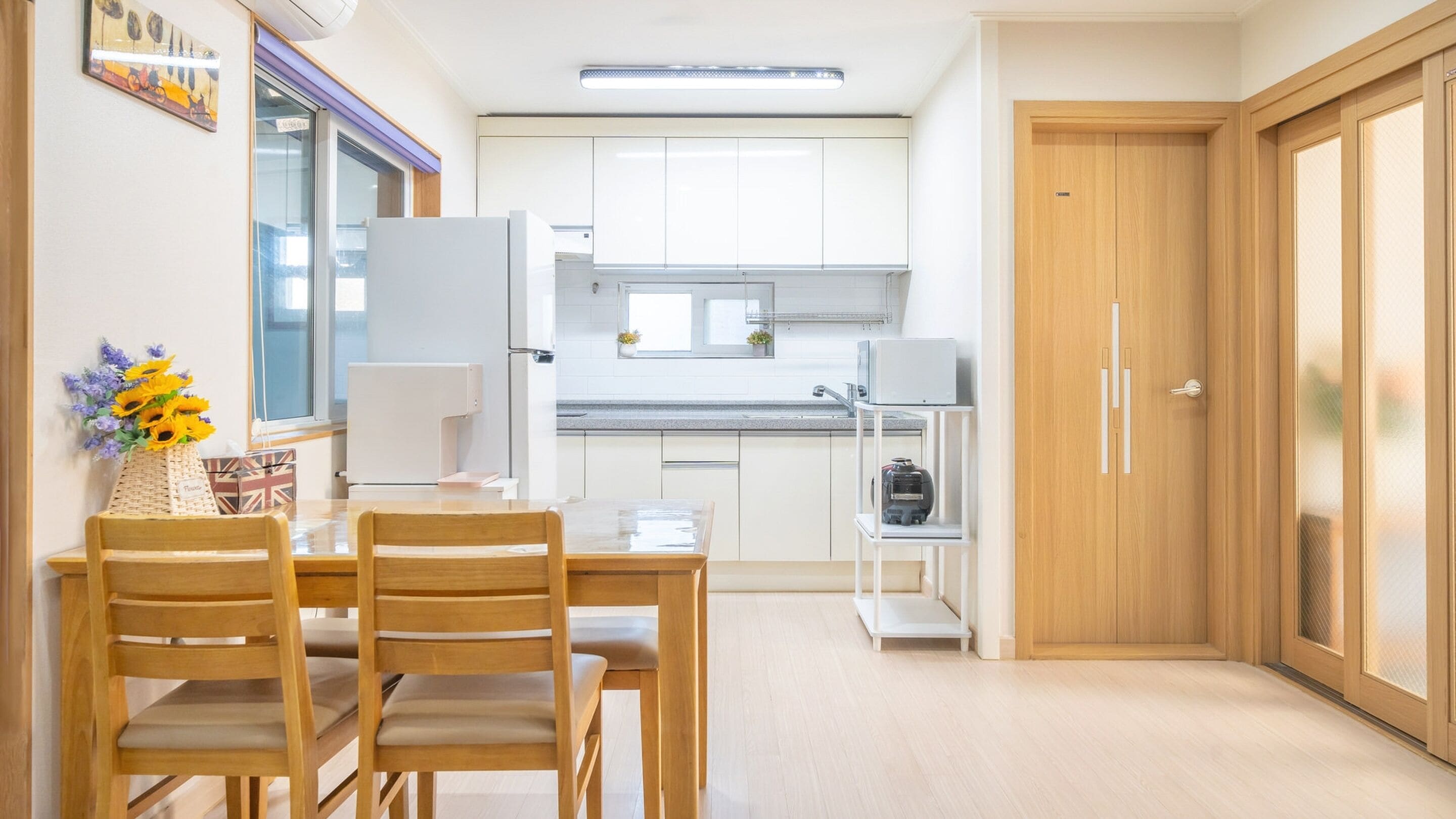 A modern kitchen with white cabinets, a built-in oven, and a microwave. There is a dining table with chairs and a vase of flowers.