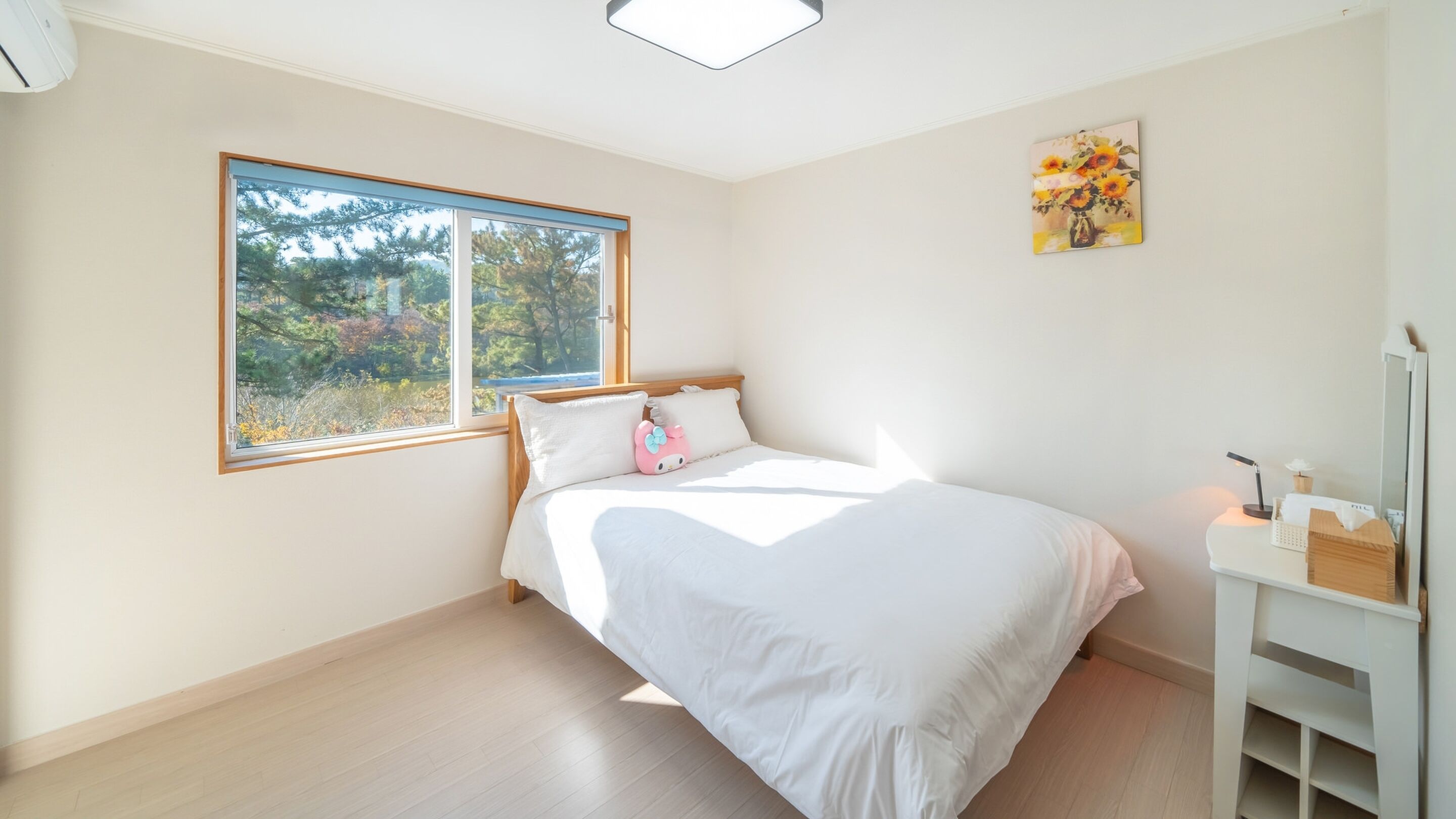 Un dormitorio con un ventanal grande, una cama con ropa de cama blanca, una almohada rosa y un cuadro en la pared.