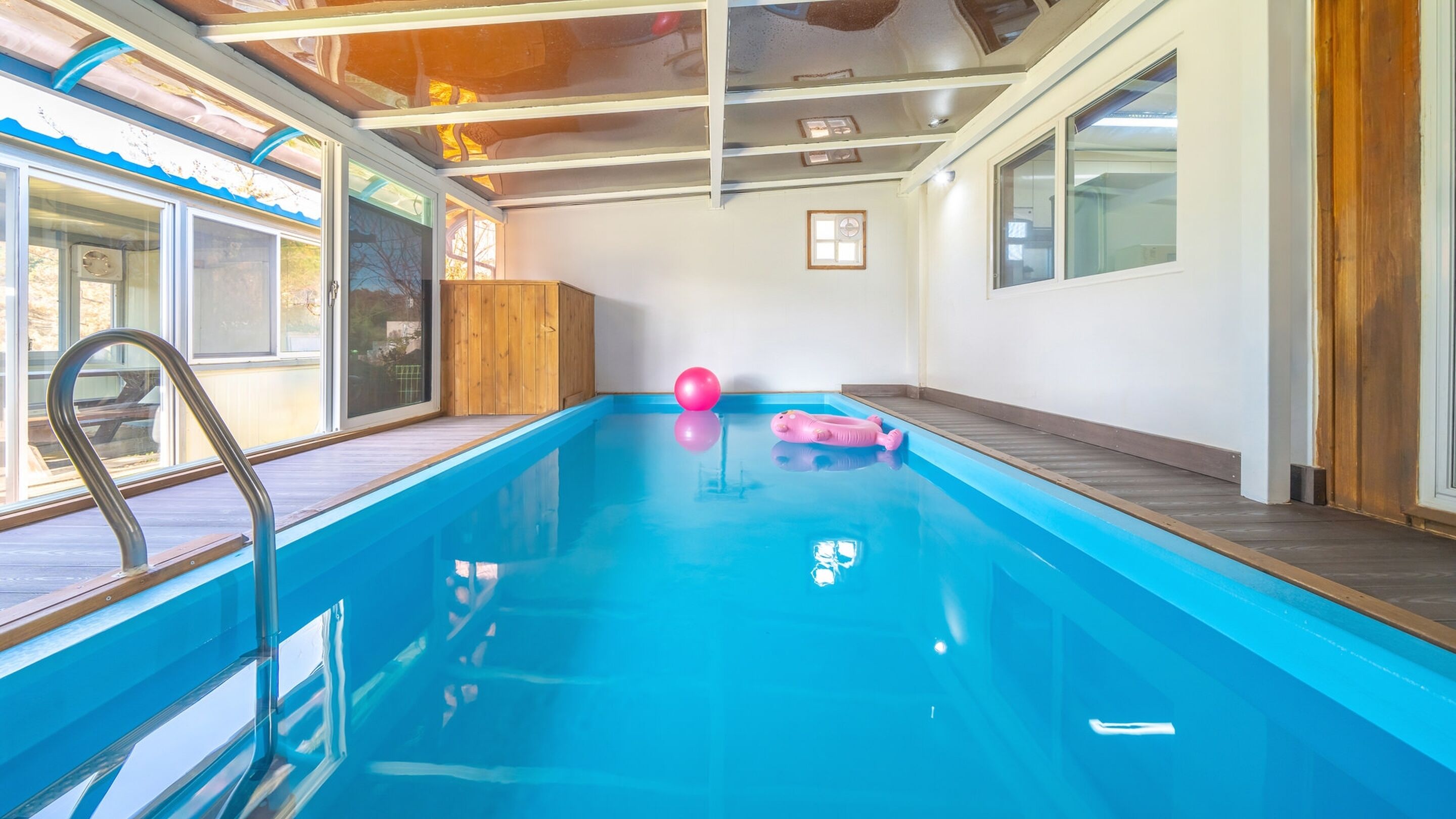 Una piscina interior con cubierta de madera, una escalera de metal y un juguete inflable rosa.