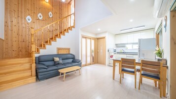 Un apartamento moderno con escalera de madera, sala de estar con sofá y mesa de centro, comedor con mesa y sillas, y cocina con armarios y electrodomésticos blancos.
