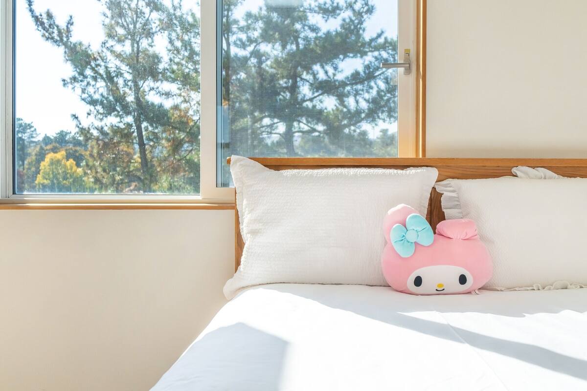 Una cama con ropa de cama blanca y un cojín rosa con lazo azul.