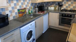 A compact kitchen with a washing machine, a sink, a stove, and a coffee maker. - NEW Super 2BD Flat near Dalkeith Town Centre (Midlothian)