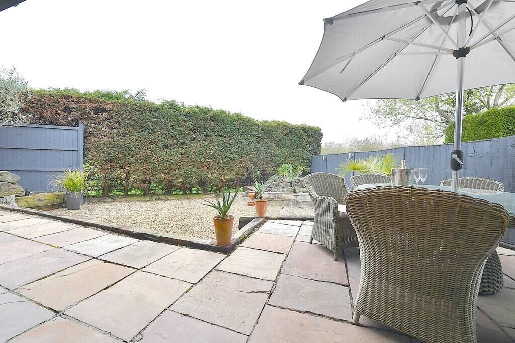 Un patio al aire libre con suelo de piedra, mobiliario de mimbre y un gran paraguas.