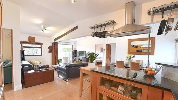 A modern kitchen with a central island, wooden cabinets, and a stainless steel range hood. - Gorgeous 3BD Cottage with Parking Nr Guildford (Surrey)
