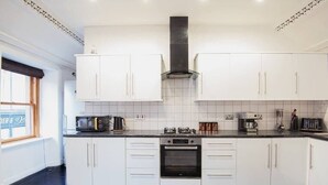A modern kitchen with white cabinets, a black stove, and a window with a view. - Charming 2 Bedroom Flat in the Heart of Kirriemuir (Angus)