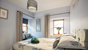 A bedroom with a bed, a window with curtains, a mirror, and a lamp. - Charming 2 Bedroom Flat in the Heart of Kirriemuir (Angus)