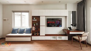 A modern living room with a built-in TV, a sofa, a desk, and a chair. - HoLo Central Hanoi - Serviced HomeStay (Hanoi)