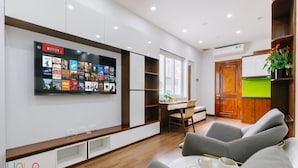 A modern living room with a flat-screen TV displaying Netflix titles, a dining area with a table and chairs, and a kitchen with a green countertop. - HoLo Central Hanoi - Serviced HomeStay (Hanoi)
