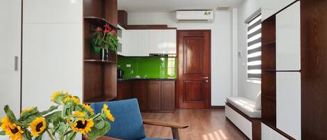 Une cuisine moderne avec des meubles blancs, un pare-feu vert et un plancher en bois. On y trouve une chaise bleue et un vase avec des tournesols.