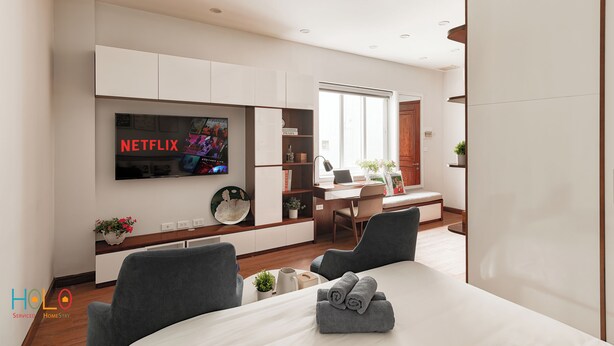 A modern hotel room with a large bed, a desk with a laptop, a television mounted on the wall, and a dining area with a table and chairs. - HoLo Central Hanoi - Serviced HomeStay (Hanoi)