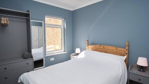A bedroom with a bed, a wardrobe, a window, and a nightstand with a lamp.