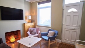 A cozy room with a fireplace, a flat-screen TV, a table, two chairs, and a large window.