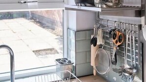 A kitchen with a clock, pots, pans, and utensils on shelves.