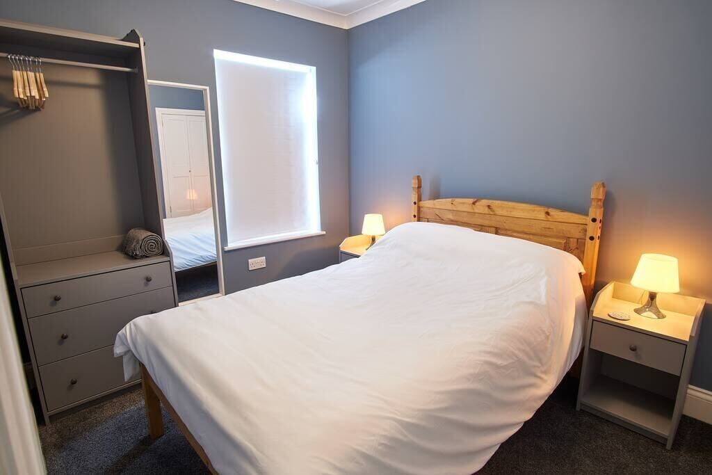 A bedroom with a bed, bedside lamps, a wardrobe, and a window.