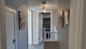Un couloir menant à un escalier, avec vue sur un balcon et un coin repas.