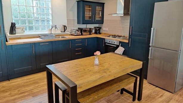 Une cuisine moderne avec des meubles de couleur bleu foncé, une table en bois et un réfrigérateur en acier inoxydable.