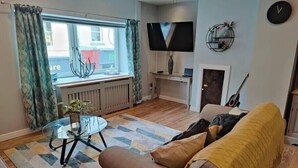 Un salon moderne avec un canapé, une table basse en verre, un téléviseur et une guitare.