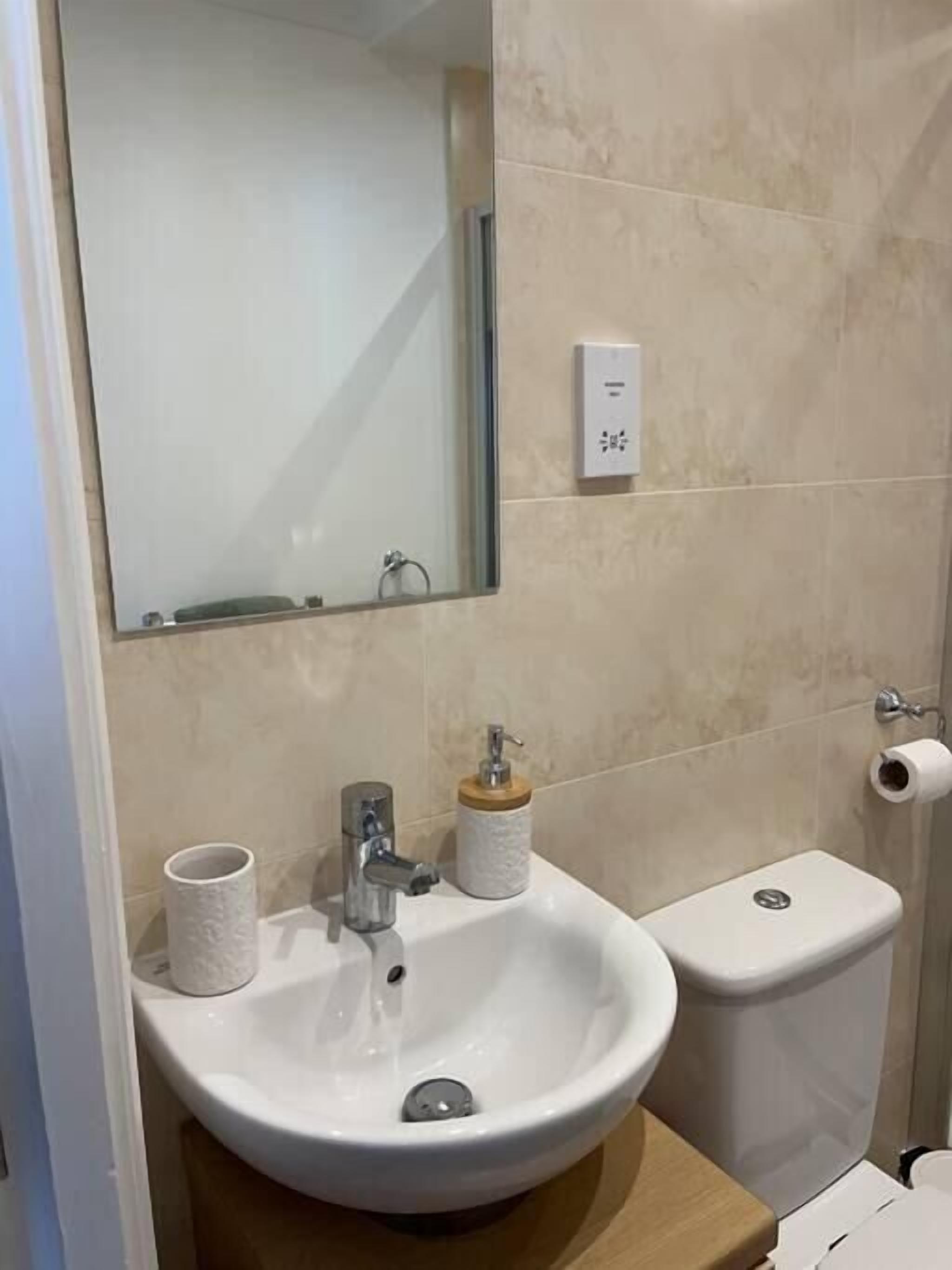 A bathroom with a white sink, a mirror, a toilet, and a soap dispenser.