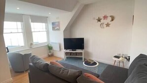 A modern living room with a large gray sectional sofa, a flat-screen TV, and a small side table.