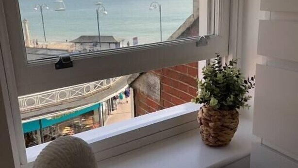 A window with a view of the sea and a building across the street.