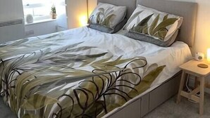 A modern bedroom with a large bed, a bedside table, a nightstand, and a painting on the wall.
