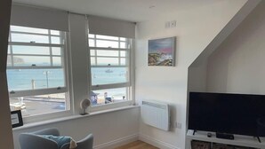 A modern living room with a large window overlooking a harbor, a flat-screen TV on a stand, and a cozy seating area.