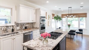 A modern kitchen with white cabinetry, granite countertops, stainless steel appliances, and a central island with seating. - New! Chic Cottage Home W/ Backyard Pool - 12 min to the River Walk! (Alamo Heights)