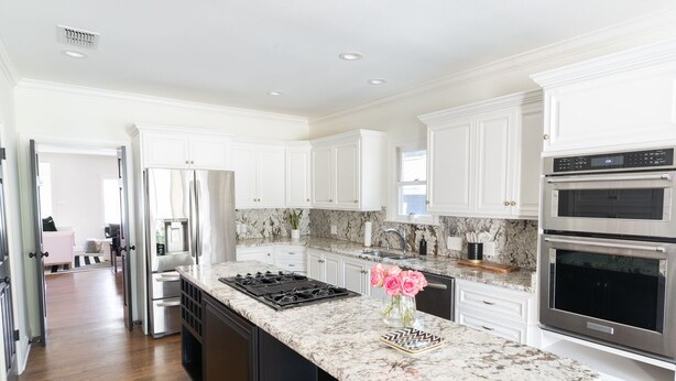A modern kitchen with white cabinetry, a granite countertop, stainless steel appliances, and a central island with a gas stove. - New! Chic Cottage Home W/ Backyard Pool - 12 min to the River Walk! (Alamo Heights)