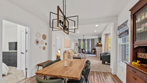 A spacious dining area with a wooden table and chairs, a chandelier, and a view into the living room. - The Suncatcher- Steps to Lake Michigan. Pet Friendly & Fully Fenced (Sheboygan)