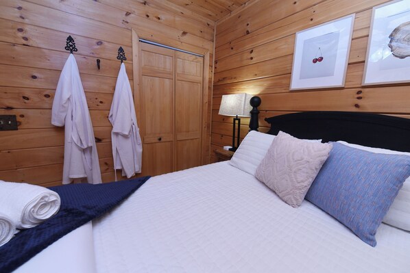 A wooden-paneled room with a bed, towels, a nightstand, and framed pictures on the wall.