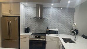 Una cocina moderna con electrodomésticos de acero inoxidable, salpicadero con diseño de ladrillo y encimera blanca.