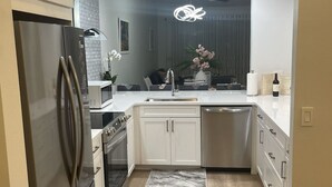 Una cocina moderna con un refrigerador de acero inoxidable, un microondas, un horno, un lavamanos y un lavavajillas. Hay una alfombra en el suelo con diseño de mármol.