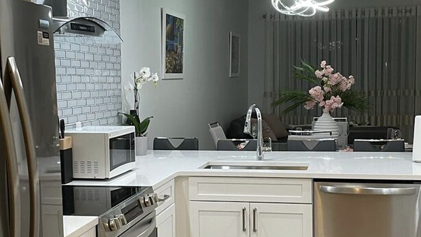 Una cocina moderna con armarios blancos, electrodomésticos de acero inoxidable, salpicadero de mármol y una isla central con fregadero.