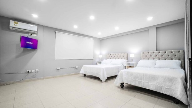 Habitació d'hotel amb dos llits, televisió, aire condicionat i pantalla de projector.