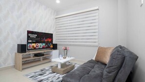 Un saló modern amb un sofà gris, una taula de centre blanca i una televisió sobre un moble de fusta.