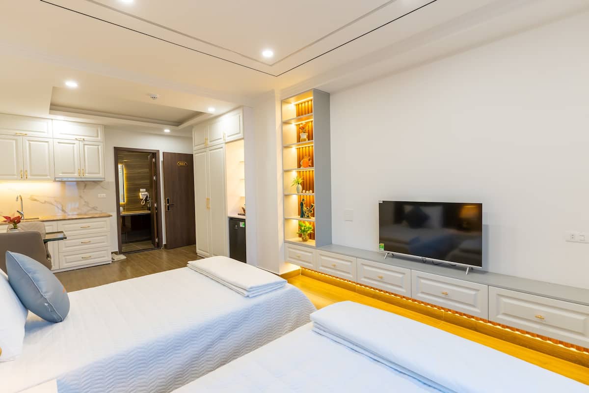 A modern hotel room with two beds, a TV, a minibar, and a bathroom.