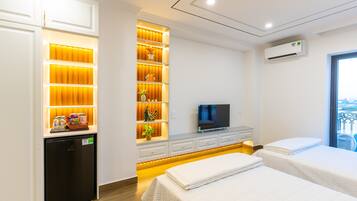 A hotel room with a bed, a TV, a mini-fridge, and a built-in shelf with decorative items.